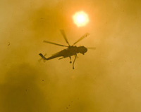 a still from Olympia: What's Next?: a firefighting helicopter flies overhead, shrouded in smoke